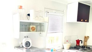 A compact kitchen with a built-in stove, a small sink, and a window with blinds. - Cozy tiny house in nature, 5 mins from Beach | With sea view & high speed WiFi (Tarifa)