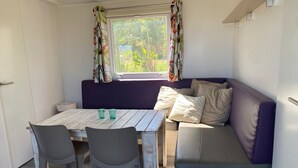 A compact living space with a wooden table, two chairs, a purple sofa, and a window with curtains. - Cozy tiny house in nature, 5 mins from Beach | With sea view & high speed WiFi (Tarifa)