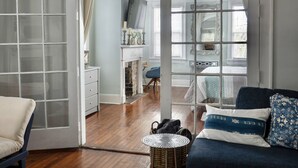 Een ruime woonkamer met een grote, rondbogen doorgang naar een andere kamer, een blauwe bank, een witte fauteuil en een houten salontafel.