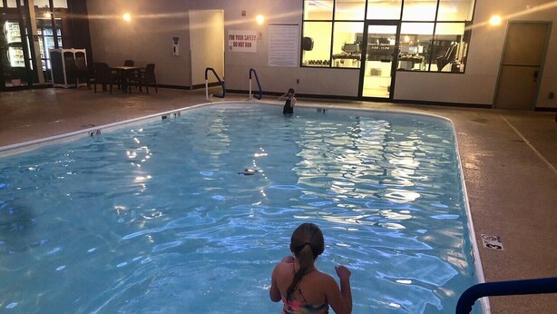 An indoor swimming pool with a person in the water, poolside seating, and a safety sign on the wall. - FALLS - Shop Till You Drop, Then Relax in a Comfortable Studio Suite (Branson)