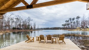 Une terrasse en bois, agrémentée de chaises et de tables, qui offre une vue sur un lac et est entourée d’arbres.