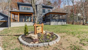 Une maison moderne à deux étages, dotée d’une façade en pierre, de grandes fenêtres et d’un jardin bien entretenu à l’avant, avec une plaque indiquant le nom de la propriété.