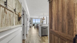 A hallway leading to a kitchen with a wooden wall, a chandelier, and a view of the ocean. - Emerald Isle 506 - Beautiful beachfront condo! Front row chairs included! (Panama City Beach)