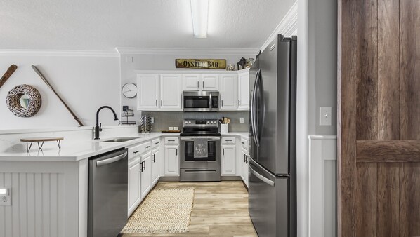 Una cocina moderna con armarios blancos, electrodomésticos de acero inoxidable y una pared decorativa de madera.