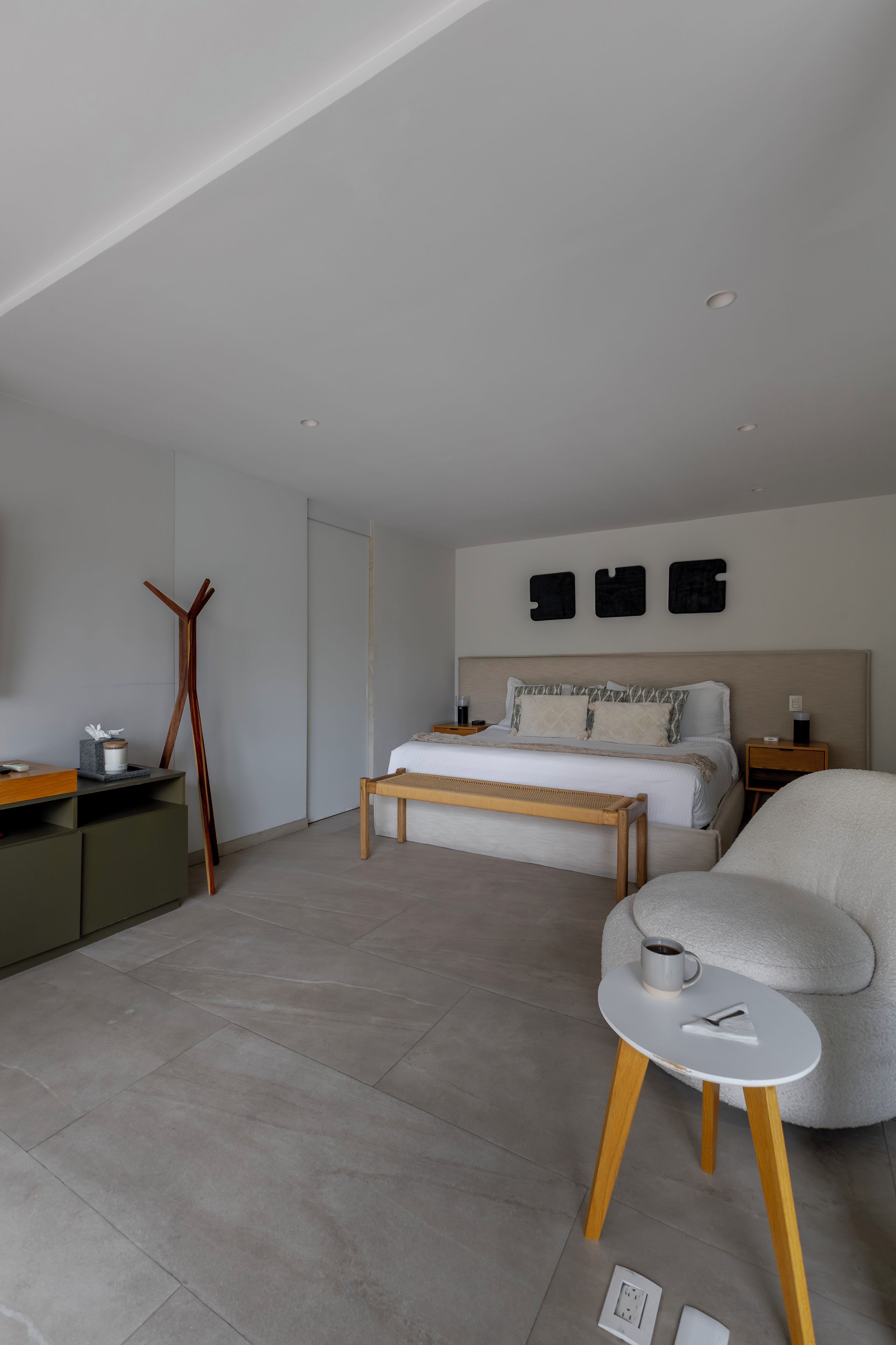 Ein modernes Schlafzimmer mit Bett, Nachttischen, einer Bank, einem Sessel und einem Schreibtisch.