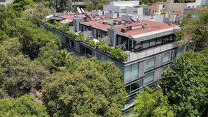 A modern multi-story building with a rooftop terrace, surrounded by dense greenery. - Capitalia Parque Lincoln (Mexico City)