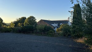 A rural landscape with a gravel road, a white house with a dark roof, and dense greenery. - Herdwick Inn (Penrith)