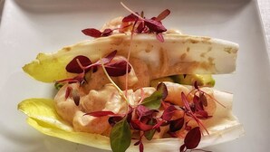 A plate with a seafood dish, possibly shrimp, on a bed of lettuce leaves, garnished with red and green microgreens. - Herdwick Inn (Penrith)