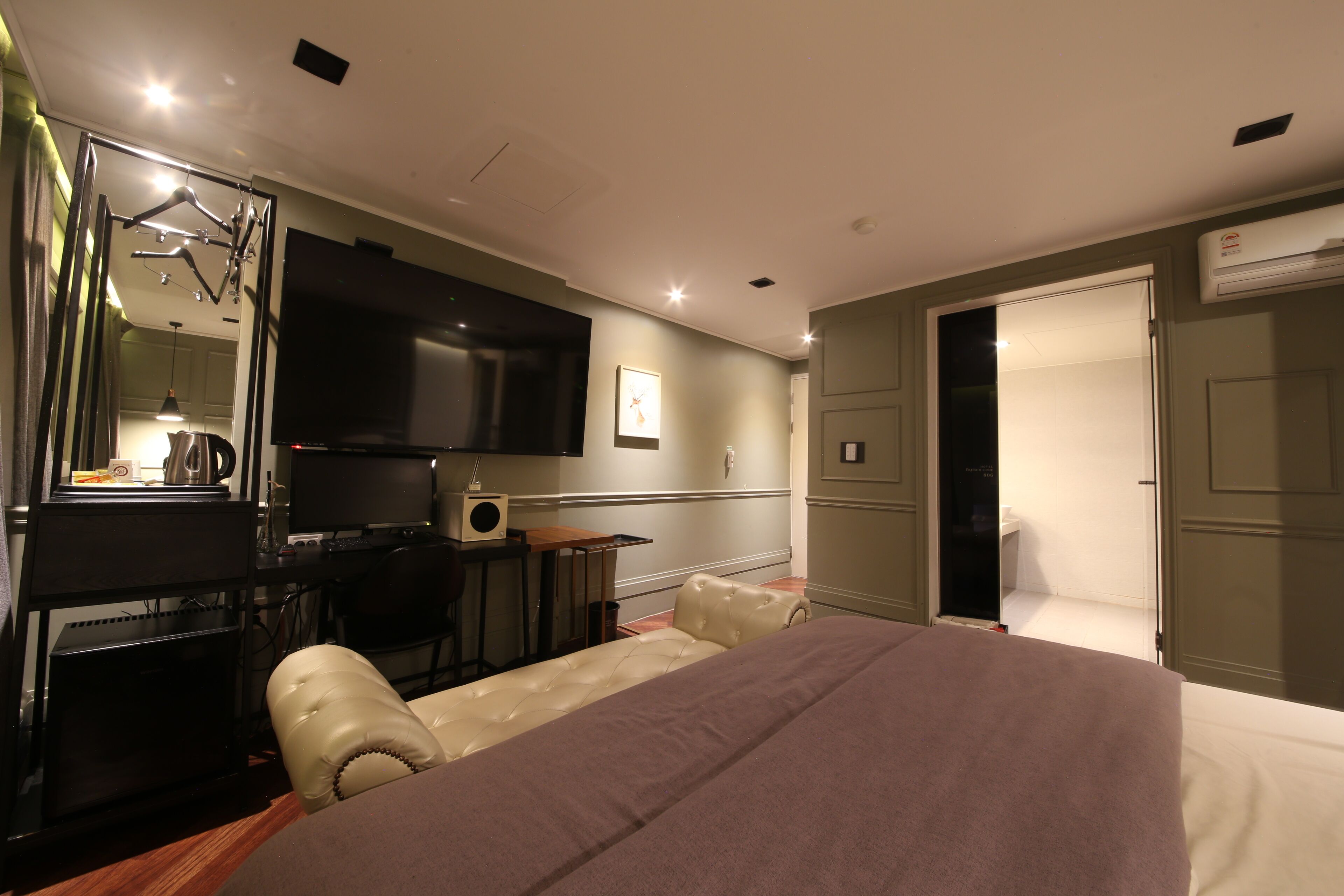 A hotel room with a bed, a desk with a computer, a chair, a TV, and a wardrobe.