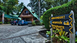 A sign with 'RECEPTION' and 'RESTAURANTE LAS GALAS' directions, a building with a green roof, and parked cars. - Hotel Villa Zurqui (San Jeronimo)