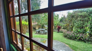 A view through a window with a stone pathway leading to a garden with a stone bench and various plants. - Hotel Villa Zurqui (San Jeronimo)