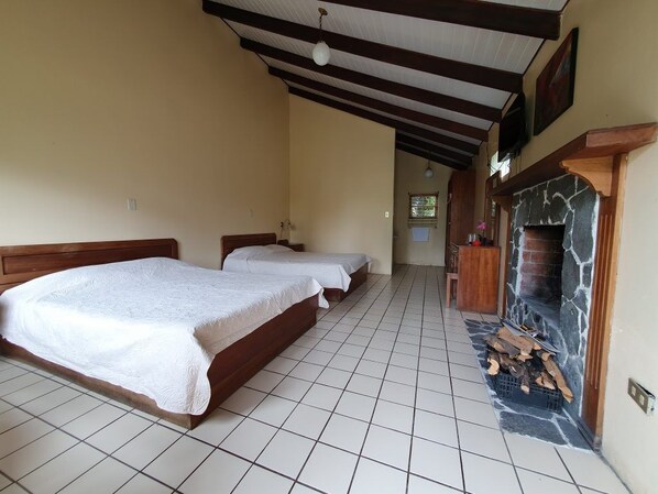 A bedroom with two beds, a stone fireplace, and a tiled floor. - Hotel Villa Zurqui (San Jeronimo)