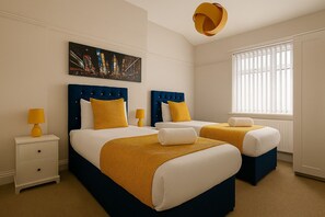 Une chambre d’hôtel avec deux lits, chacun doté d’une tête de lit bleue, de draps blancs et d’éléments décoratifs jaunes. Au-dessus des lits, on peut voir un tableau, et la chambre est équipée d’une fenêtre avec des stores et d’une lampe jaune posée sur une table de chevet.