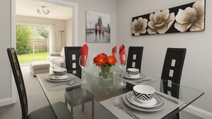 Ein Esszimmer mit Glastisch, gedecktem Tisch für vier Personen, schwarzen Stühlen und einer Vase mit roten Blumen.