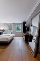 Un dormitorio moderno con cama, escritorio y televisión. Dos ventanas permiten la entrada de luz natural.