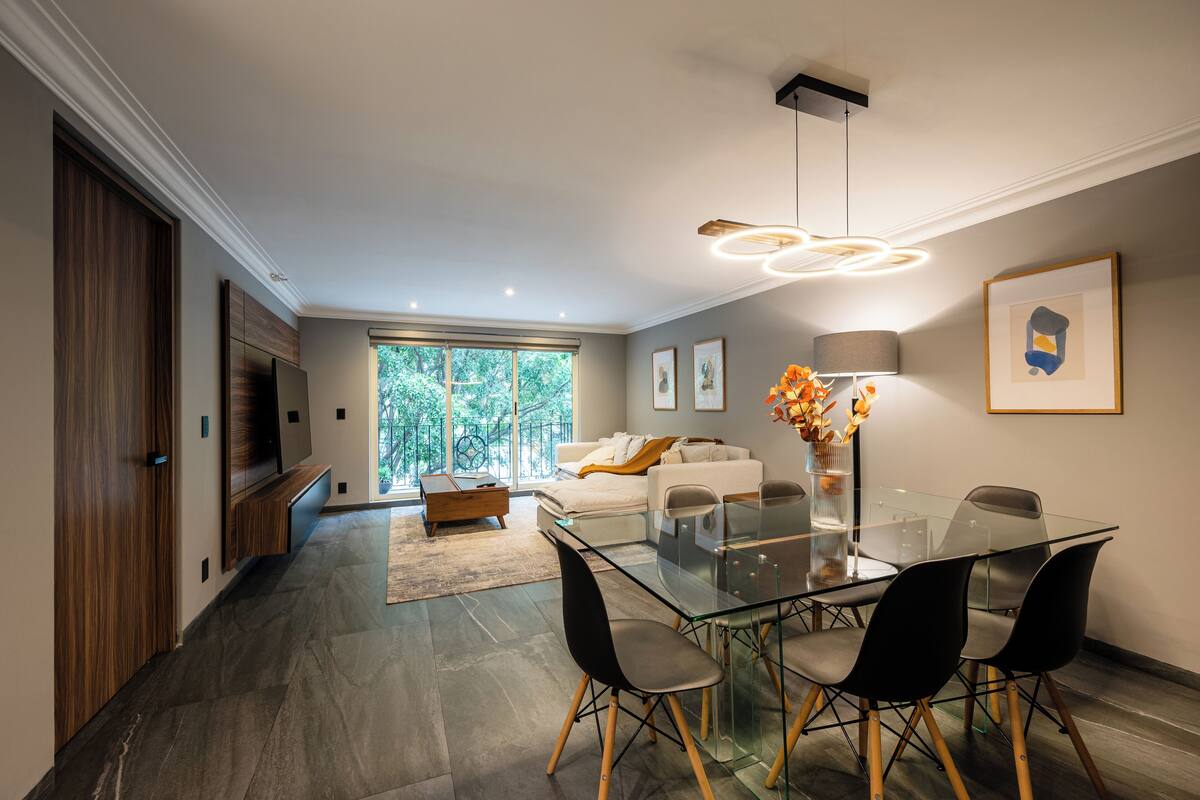 Una sala de estar moderna con una mesa de comedor de vidrio, sillas negras, un sofá y un ventanal grande.