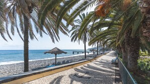 A paved walkway with palm trees, a beach, and a thatched-roof structure. - Casa Morena by Atlantic Holiday (Santa Cruz)