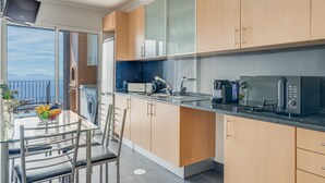 A modern kitchen with wooden cabinets, a granite countertop, and a view of the sea through large windows. - Casa Morena by Atlantic Holiday (Santa Cruz)