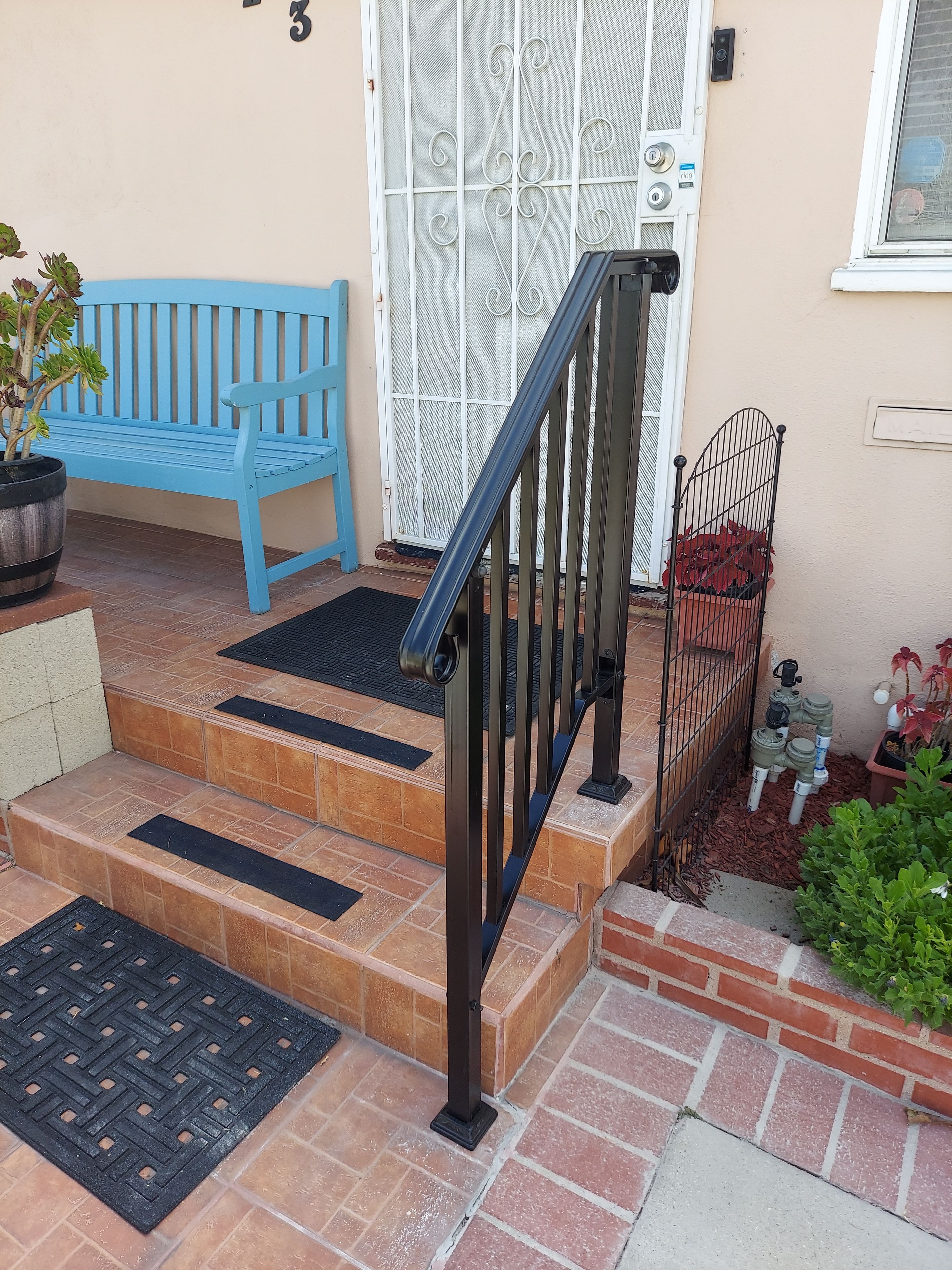 A set of outdoor steps leading to a door with a metal gate, a blue bench, and potted plants.