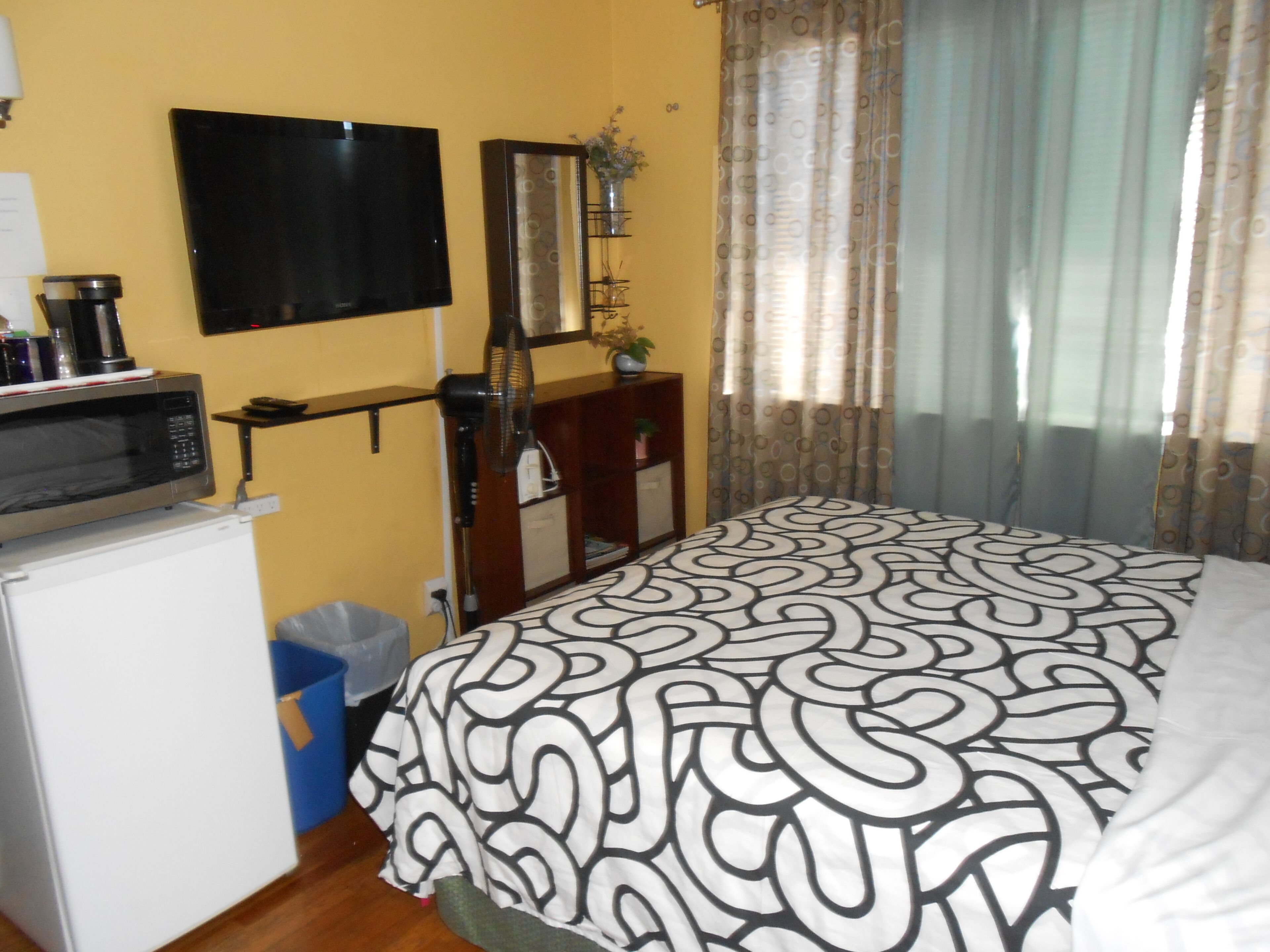 A bedroom with a bed, a television, a microwave, and a small trash bin.