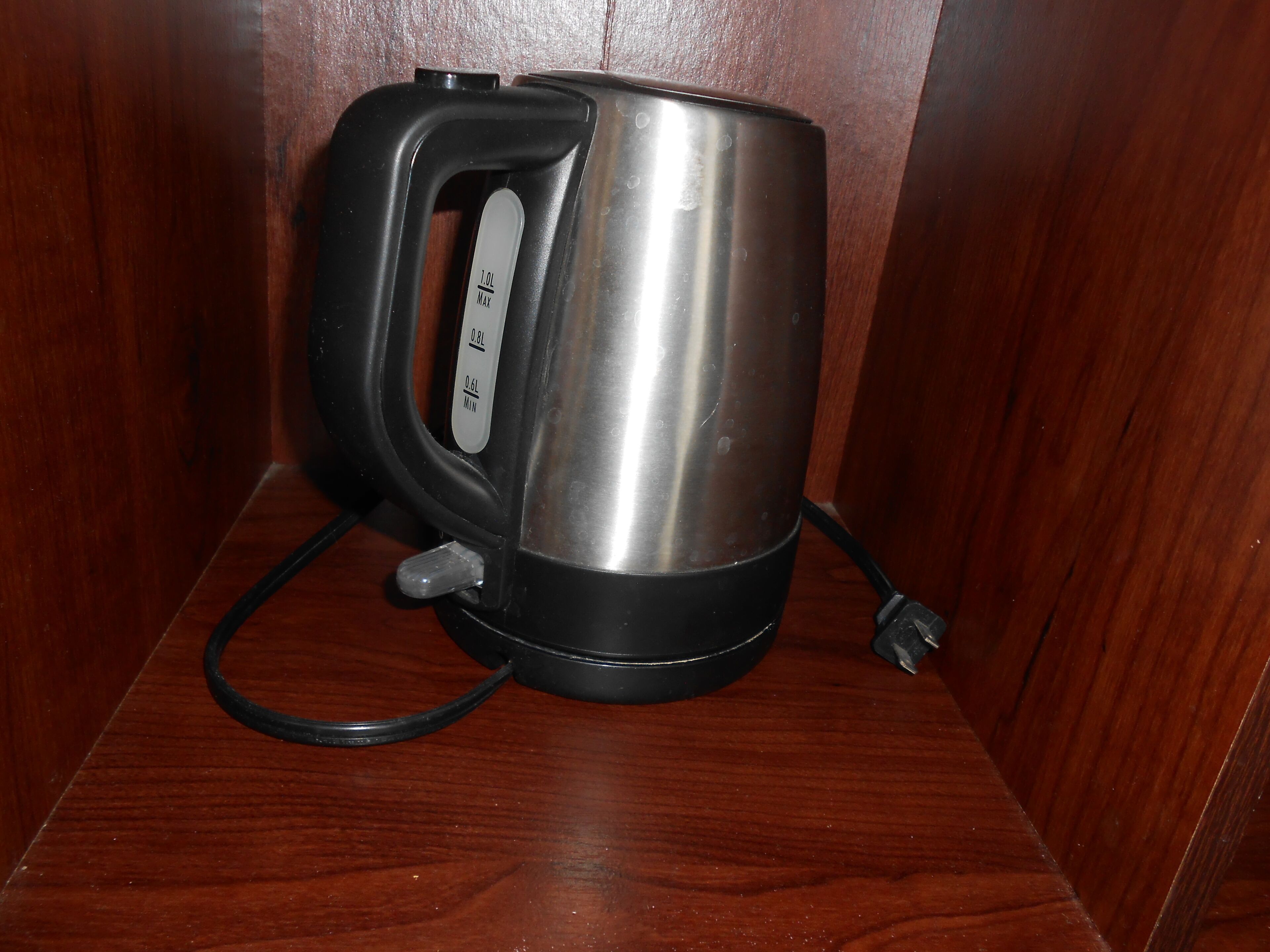 Una tetera eléctrica de acero inoxidable con un asa y cable negros, sobre una superficie de madera.