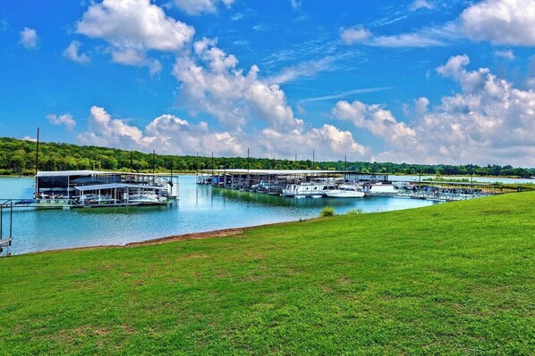 A marina with boats docked, a grassy area in the foreground, and a bridge in the background.