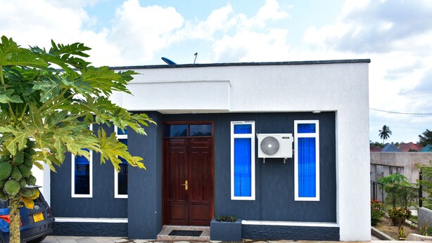 Une maison moderne avec une façade sombre, une porte marron et un petit jardin à l’avant.