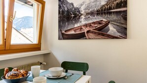Comedor con una mesa preparada para dos, un bol de pasteles y un cuadro de un lago de montaña con barcos.