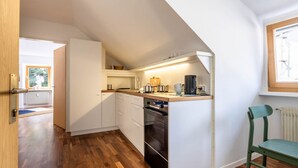 Una cocina compacta con armarios blancos, horno integrado y cafetera.