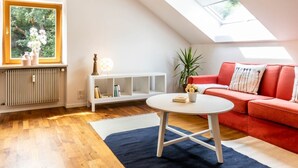 Una sala moderna con tragaluz, un sof á rojo, una mesa de centro blanca y una consola blanca con libros.