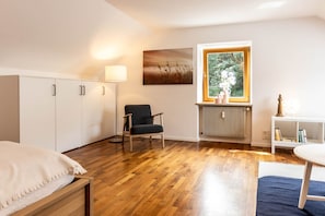 A bedroom with a wooden floor, a bed, a chair, a radiator, a window with a view of greenery, and a painting on the wall. - Central Attic Castle View with private parking (Brunico)