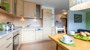 Une cuisine moderne avec des meubles de couleur bois clair, un four encastré et un coin repas avec une table dressée pour deux personnes.