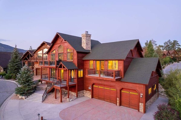 A large, multi-story wooden house with a balcony, a garage, and a chimney.