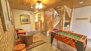 A cozy room with a foosball table, a wooden staircase, and a dining area with a table and chairs. - Windsong Retreat | 3X2 PROMO | Lake Views. Hot tub (Big Bear Lake)