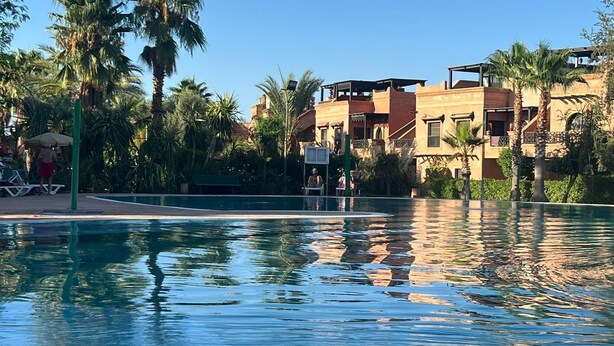 En swimmingpool med kristallklart vatten, omgiven av palmer och byggnader med traditionell arkitektur.