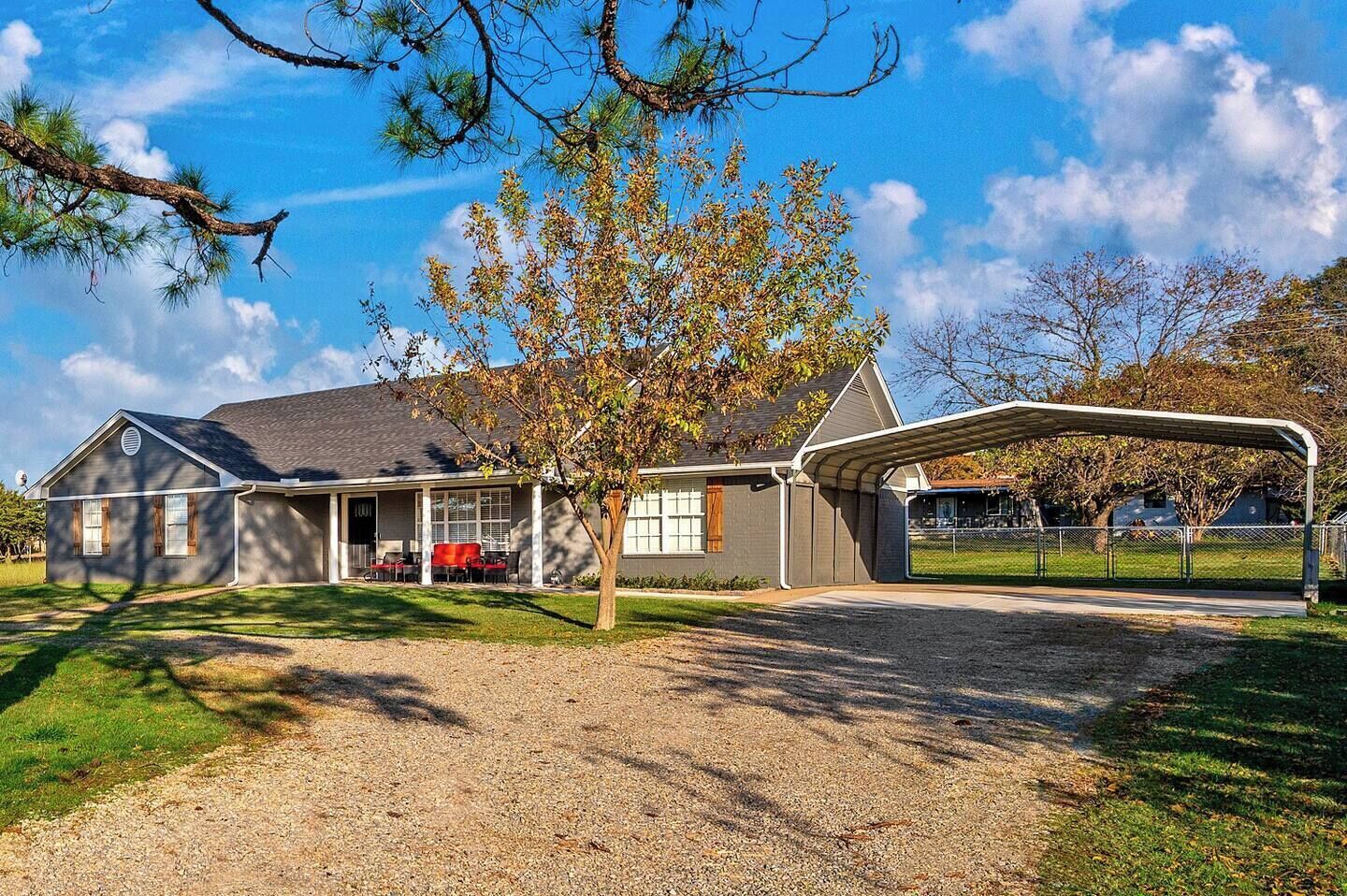 A two-story house with a covered porch, a gravel driveway, and a tree in the foreground.