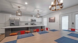 A modern kitchen with white cabinets, a stainless steel refrigerator, a microwave, and a coffee maker. There is a dining table with blue placemats and red chairs. - Best kitchen in Texoma! New! Playroom! (Mead)