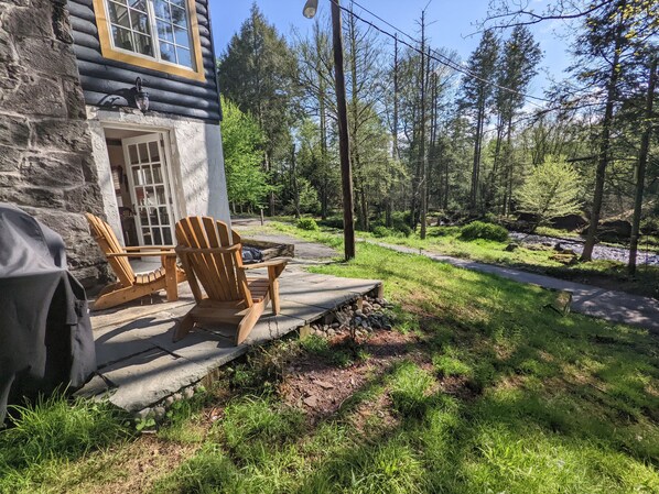 Une cabane avec une façade en pierre, une terrasse en bois et deux chaises Adirondack.