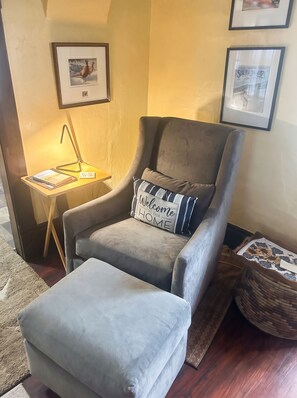 Un fauteuil gris avec un coussin à rayures, une petite table d’appoint avec une lampe et un tableau encadré au mur.