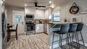 Una cocina moderna con armarios blancos, microondas integrado, horno y una barra con taburetes.