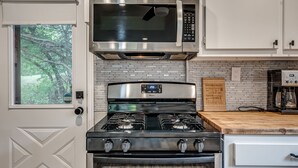 Una cocina con microondas de acero inoxidable, estufa a gas y horno empotrado. Hay una ventana con vistas a árboles, y una encimera de madera.