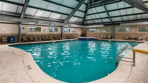 Une piscine intérieure à l’eau claire, dotée d’un plongeoir et de plusieurs espaces aménagés pour s’asseoir le long des bords.