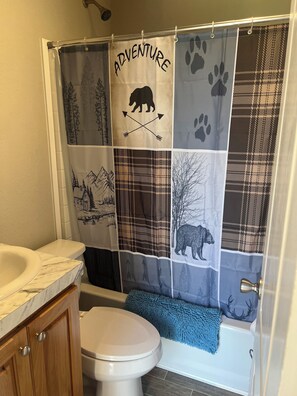 A bathroom with a shower curtain featuring a bear and mountain design, a white toilet, and a blue bath mat.