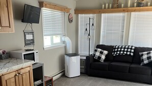 A modern living room with a black sofa, a white air purifier, and a kitchen area with a microwave.
