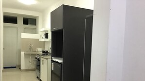 Une cuisine de taille réduite avec des meubles blancs, un réfrigérateur noir et un évier.