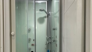 Une cabine de douche fermée par des parois en verre, équipée d’un pommeau de douche à main, d’un flexible de douche et d’un robinet mural.