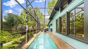 A pool area with a glass enclosure, surrounded by plants and a wooden fence. - Unique house - heated pool and hot tub option near Clearwater Beach Florida (Clearwater)