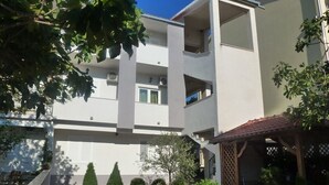 Un edificio residencial de varios pisos con balcones, un patio cubierto y un pequeño jardín con arbustos y un árbol.
