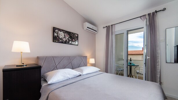 Habitación de hotel con cama, mesita de noche, lámpara, aire acondicionado instalado en la pared, un cuadro y puerta corredera de vidrio que da a un espacio exterior.