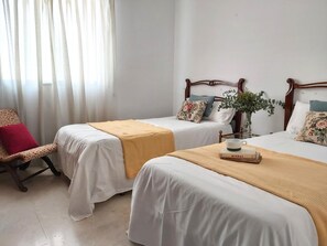 Habitación de hotel con dos camas individuales, una silla y una mesita de noche con un libro y una taza.